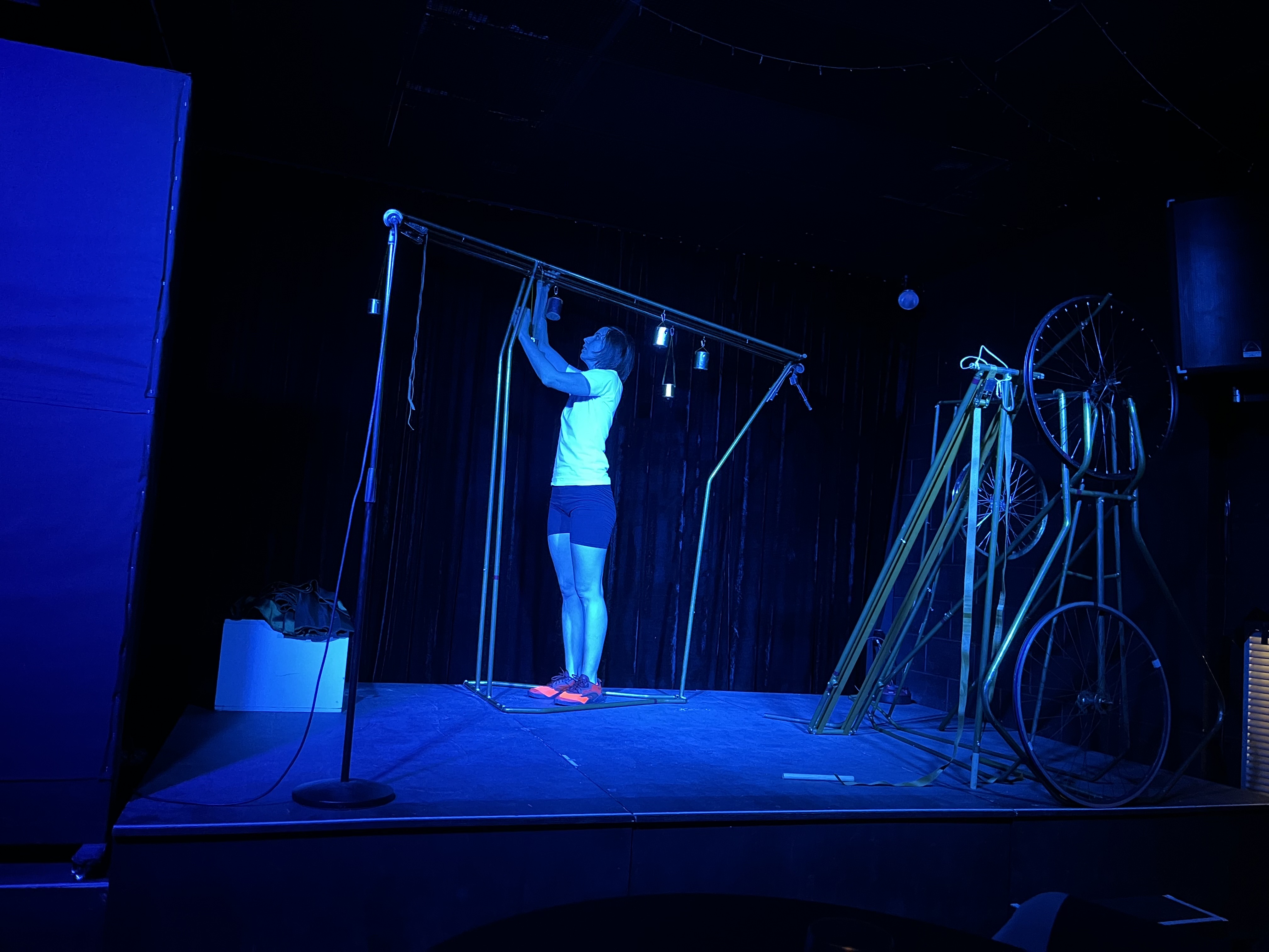 Actor Miranda Prag assembles a metallic structure onstage, under deep blue lighting
